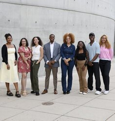 A group of 8 LAF Ignite students stand in front of a curved concrete wall.