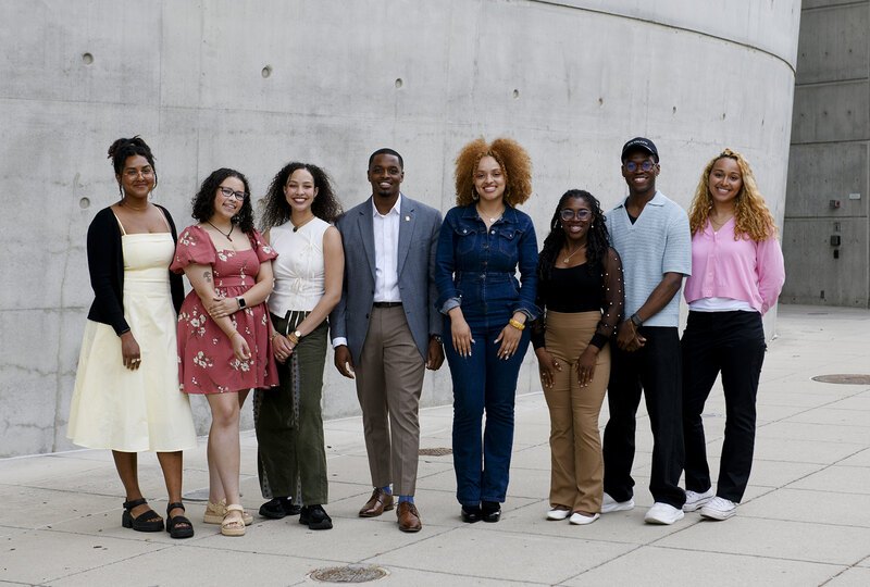 A group of 8 LAF Ignite students stand in front of a curved concrete wall.