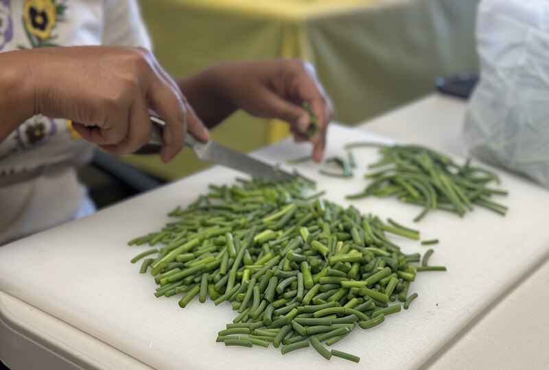 A pile of coarsely chopped wild ramps on a cutting board with the two hands and knife that are chopping the ramps