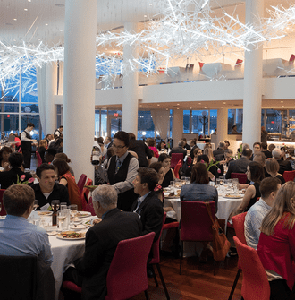 A lively room full of guests seated at tables enjoying dinner