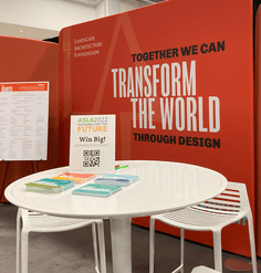 LAF EXPO booth with a white table and postcards in front of a coral red backdrop 